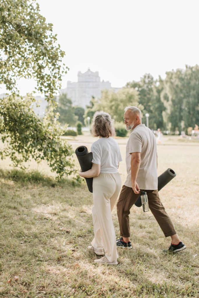 Elderly couple walking in park carrying yoga mats for a wellness session.